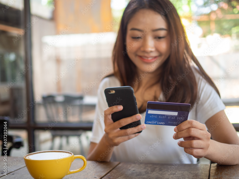 The smiling young Asian woman enjoys shopping online via a smartphone and paying online via credit card. Convenience of spending without cash. stay safe, shopping from home and Social distance The smiling young Asian woman enjoys shopping online via a smartphone and paying online via credit card. Convenience of spending without cash. stay safe, shopping from home and Social distance
