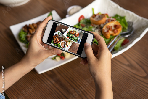 The woman hand is using a mobile phone to take a picture of food on the dining table in the restaurant. Photography with Mobile Phone Concepts
