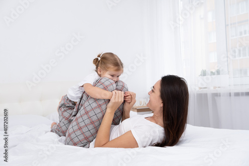 adult mother play with little active daughter in bed at home, having fun, activity with children.