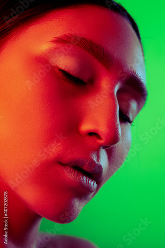 Fire. Beautiful east woman close up portrait isolated on green background in red neon light. Details, skin care and make up. Concept of human emotions, facial expression, sales, ad, fashion and beauty