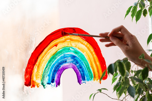 Little girl painting rainbow on window during Covid-19 quarantine at home. photo