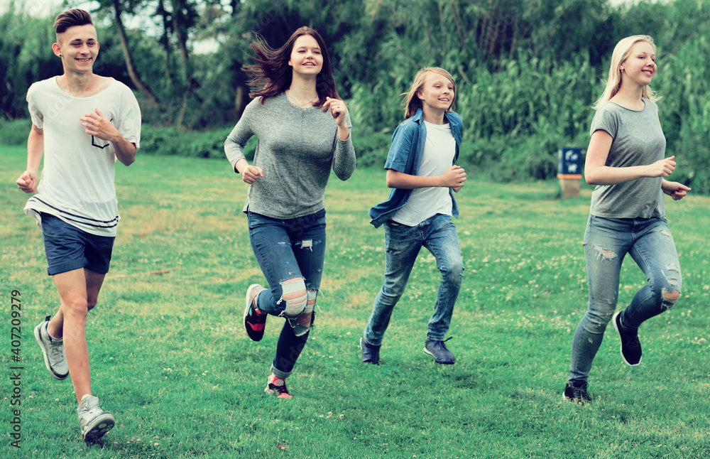 Fototapeta premium teenagers running through green lawn in summer in park