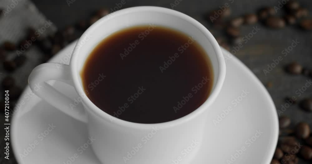 White cup of coffee with roasted coffee beans scattered on a wooden table. Mug of fresh black coffee. Fresh arabica roasted coffee beans. Great start of perfect morning. Espresso, americano, doppio. White cup of coffee with roasted coffee beans scattered on a wooden table. Mug of fresh black coffee. Fresh arabica roasted coffee beans. Great start of perfect morning. Espresso, americano, doppio.