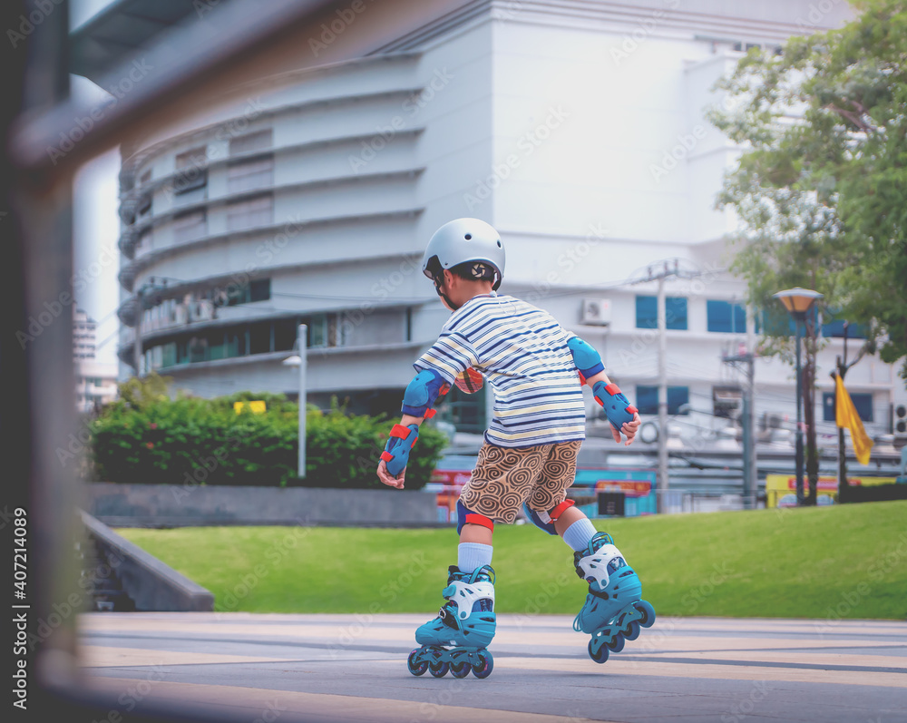 Fototapeta premium Little Asian Boy is learning to Skate on an Rollerblade in park with full protection gear and helmet.
