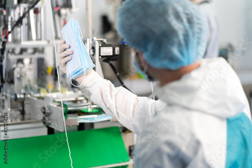 Caucasian Man worker inspecting the quality of the mask factory to in face mask production line factory. Surgical Face mask production, industry factory and people concept. indoors