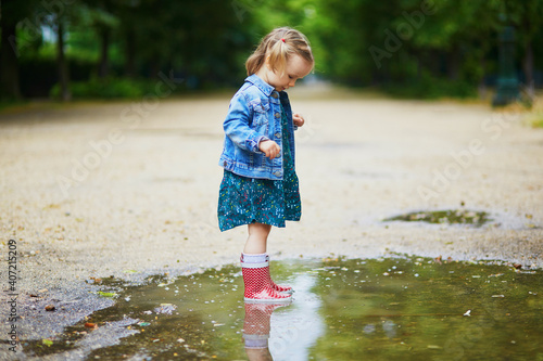 Child wearing red rain boots and jumping in puddle on a summer day