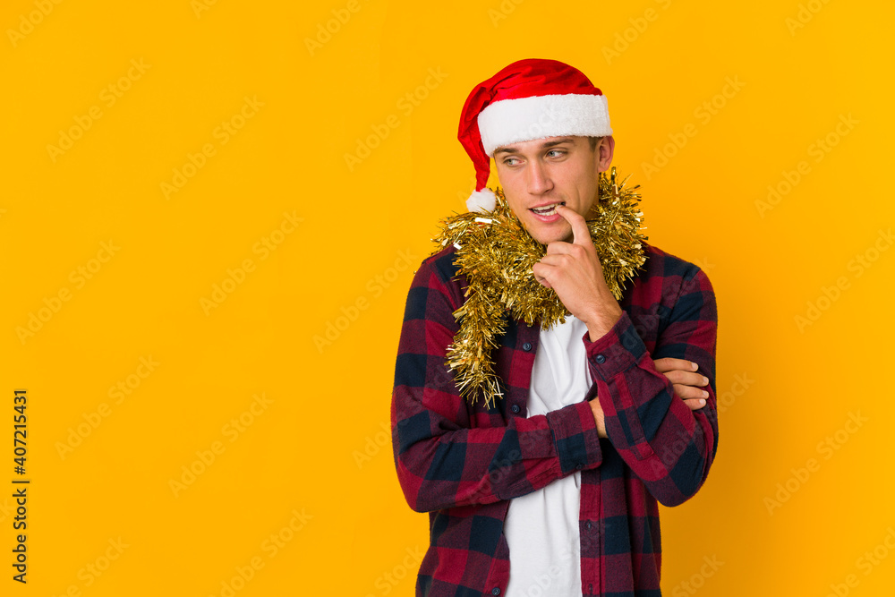 Young caucasian man with christmas hat holding a present isolated on yellow background Young caucasian man with christmas hat holding a present isolated on yellow background