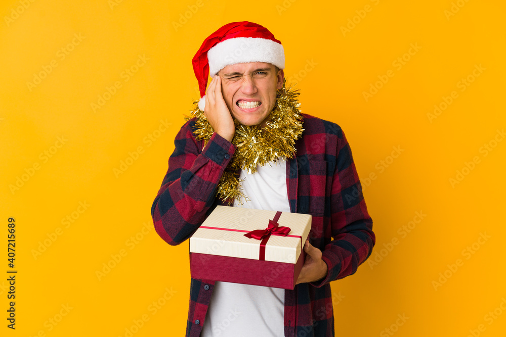 Young caucasian man with christmas hat holding a present isolated on yellow background Young caucasian man with christmas hat holding a present isolated on yellow background