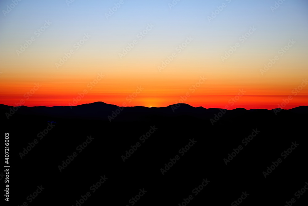Orange Sunset against black hills and blue sky.