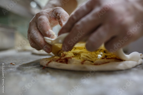 Pizzaiolo mentre chiude una pizza ripiena di ricotta e salame napoletano