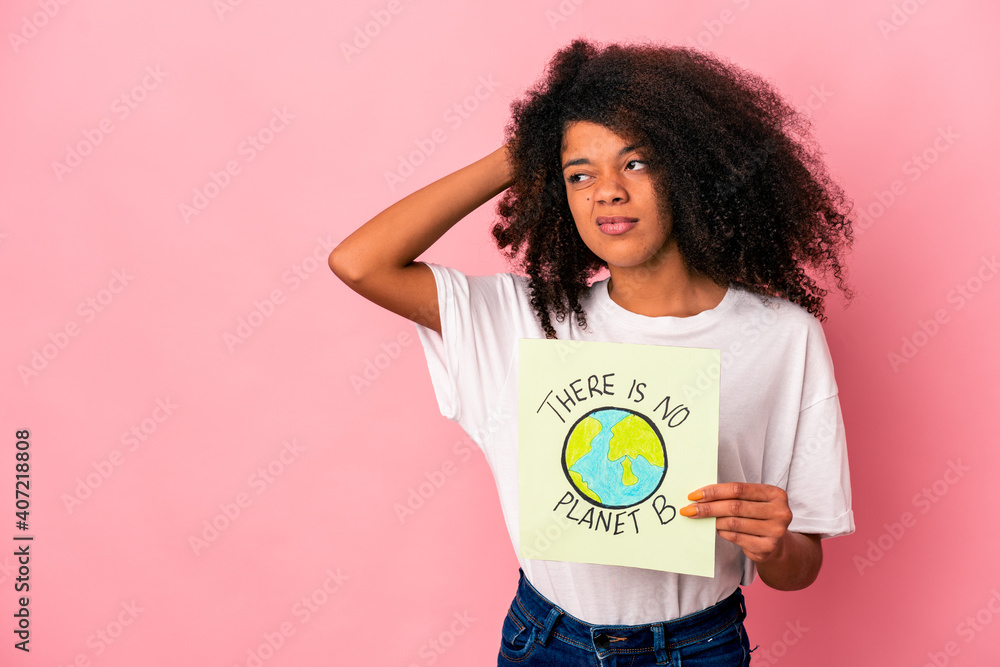 Young african american curly woman holding a planet message on a placard touching back of head, thinking and making a choice. Young african american curly woman holding a planet message on a placard touching back of head, thinking and making a choice.