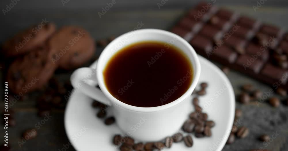Cup of coffee with cookies, chocolate and roasted coffee beans scattered on a wooden table. Black coffee mug. Fresh arabica roasted coffee beans. Great start of morning. Espresso, americano, doppio. Cup of coffee with cookies, chocolate and roasted coffee beans scattered on a wooden table. Black coffee mug. Fresh arabica roasted coffee beans. Great start of morning. Espresso, americano, doppio.