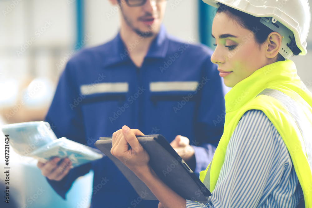 Female Inventory Manager checking stock on Digital Tablet. Man warehouse worker with hard hat safety helmet at storage buildings Female Inventory Manager checking stock on Digital Tablet. Man warehouse worker with hard hat safety helmet at storage buildings