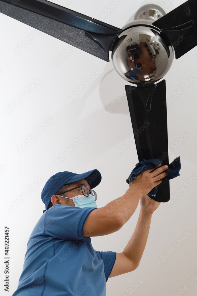 An Asian man cleaning ceiling fan at 