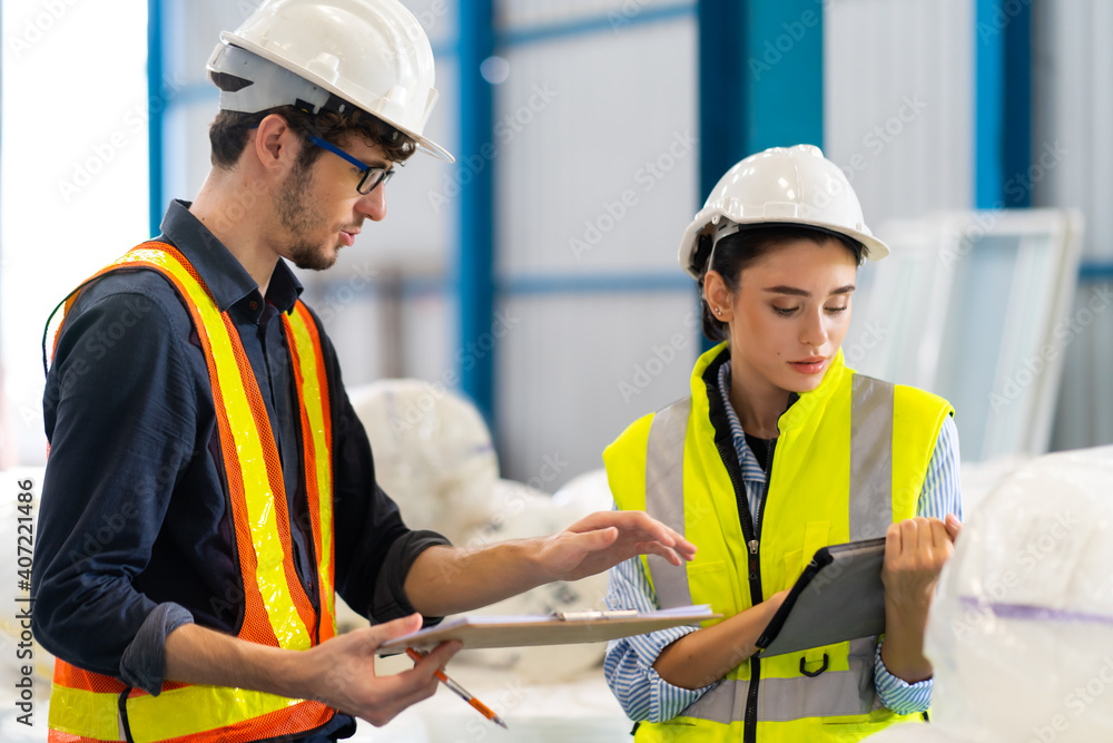 Female Inventory Manager checking stock on Digital Tablet. Man warehouse worker with hard hat safety helmet at storage buildings Female Inventory Manager checking stock on Digital Tablet. Man warehouse worker with hard hat safety helmet at storage buildings