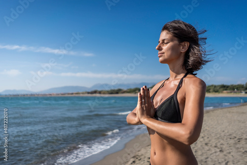 Beautiful young female doing yoga on beach. Gorgeous woman in bikini meditating on beach at summertime on vacation