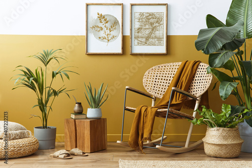 Stylish composition of living room interior with design rattan armchair, two mock up poster frames, plants, cube, palid and personal accessories in honey yellow home decor. Template. photo