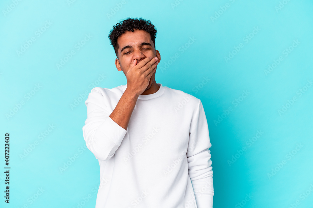 Young african american curly man isolated on blue yawning showing a tired gesture covering mouth with hand. Young african american curly man isolated on blue yawning showing a tired gesture covering mouth with hand.