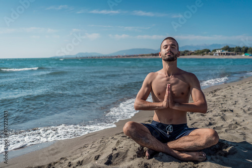 Meditation on beautiful sandy beach. Handsome young skinny man meditating and doing yoga on beach. 