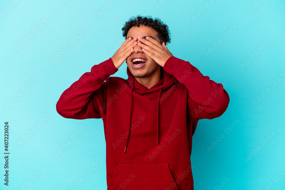 Young african american curly man isolated on blue covers eyes with hands, smiles broadly waiting for a surprise. Young african american curly man isolated on blue covers eyes with hands, smiles broadly waiting for a surprise.