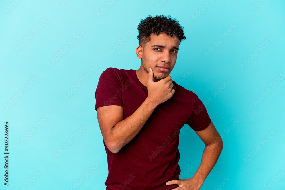 Young african american curly man isolated on blue suspicious, uncertain, examining you. Young african american curly man isolated on blue suspicious, uncertain, examining you.