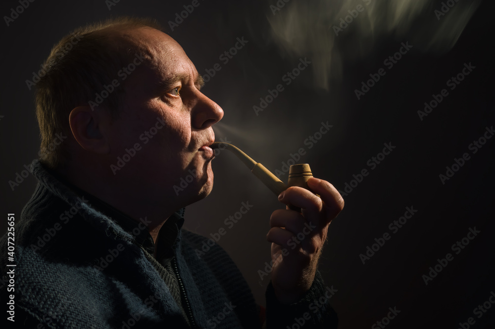 Fototapeta premium Nice portrait of a Caucasian man with tobacco pipe (side view, low key)