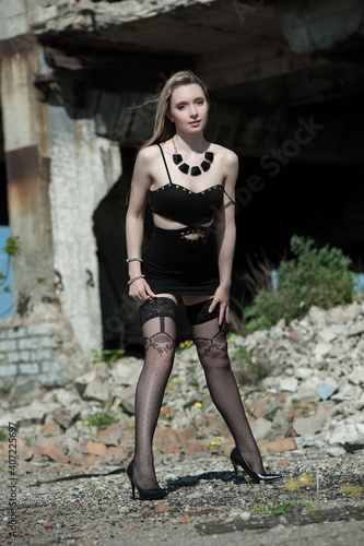 Beautiful sexy blonde girl in a black dress and stockings posing on a background of ruins © Mykola