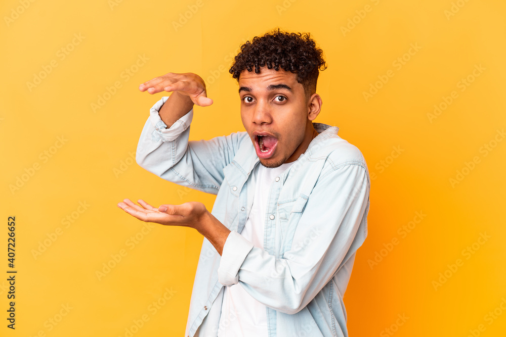 Young african american curly man isolated on purple shocked and amazed holding a copy space between hands. Young african american curly man isolated on purple shocked and amazed holding a copy space between hands.