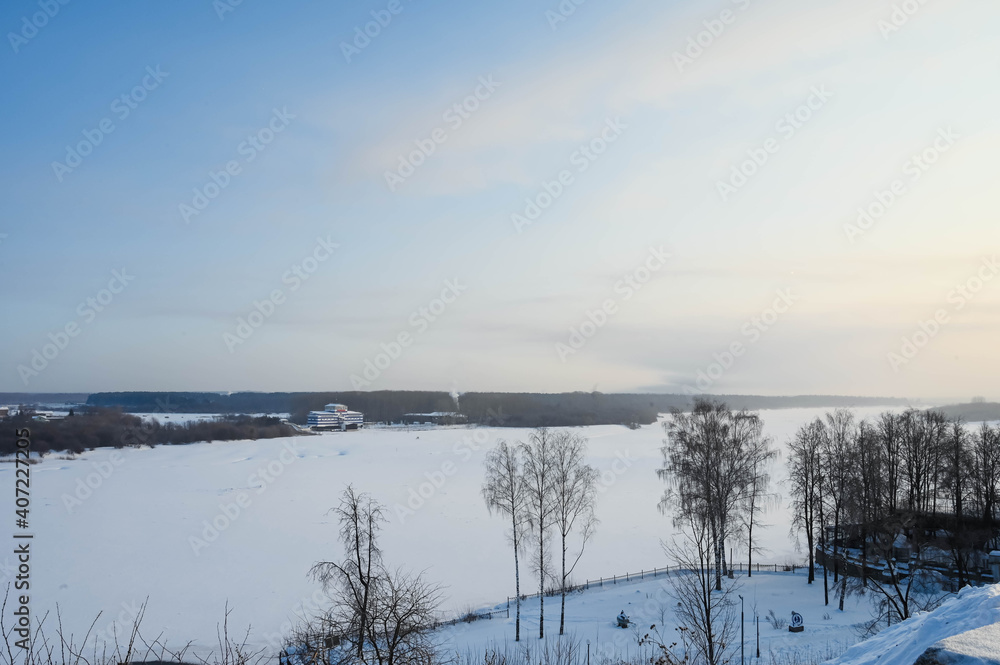 View of frozen Vyatka river at sunny winter day. Scenic russian landscape. Naked trees. A lot of snow.