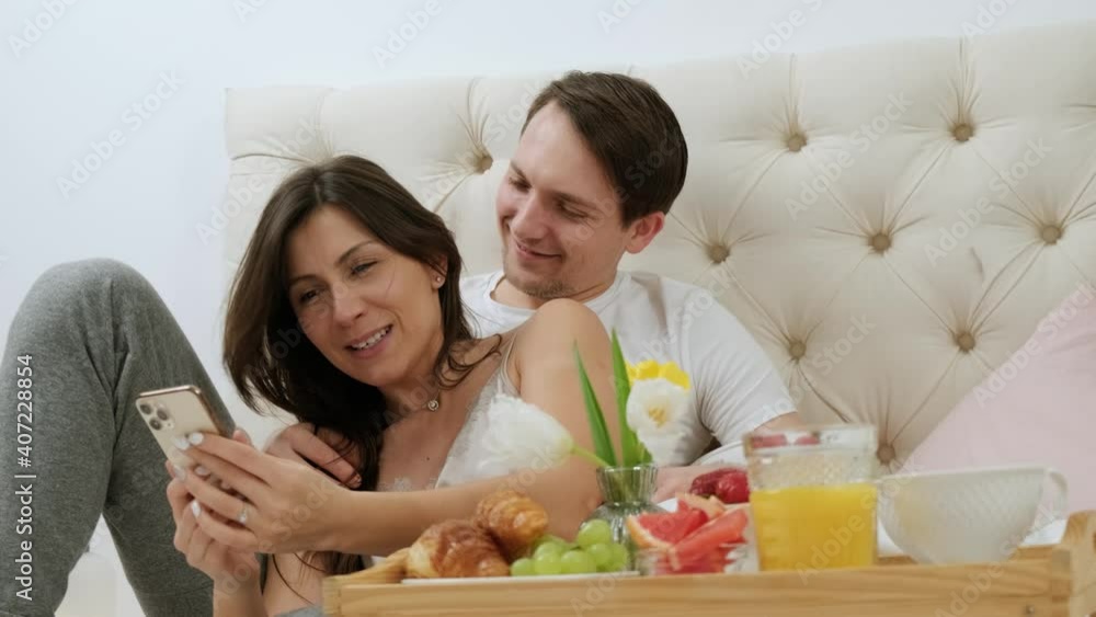 Young attractive couple taking selfie and having fun during breakfast in the bed, lying in bed, happy smile kissing, honeymoon concept, Valentine's day. Young attractive couple taking selfie and having fun during breakfast in the bed, lying in bed, happy smile kissing, honeymoon concept, Valentine's day.