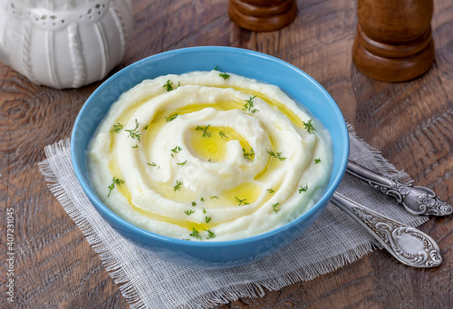 Creamy mashed cauliflower with melted butter and fresh herbs in a bowl on wooden rustic table. 