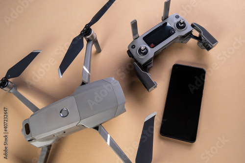 one drone, its controller and a smartphone on brown background seen from above