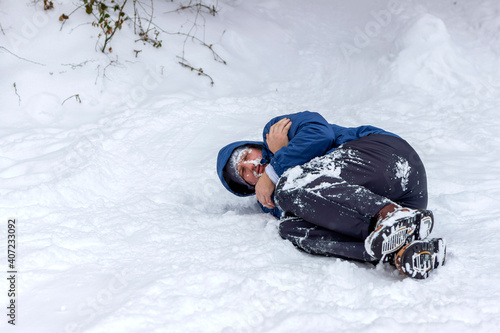 Tableau sur toile Photo of a frozen young man in blue jacket lying on the winter forest, covered snow