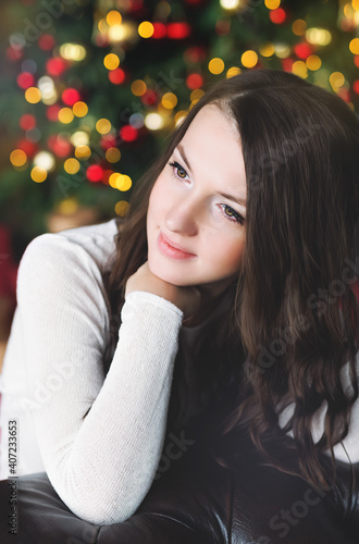 Portrait of a beautiful girl on the background of a Christmas tree with bright lights gerlant. Beautiful multicolored bokeh in the background