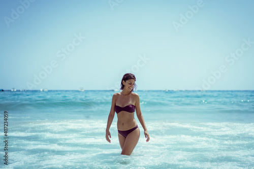 Beautiful young woman in bikini on vacation swimming in sea and enjoying in sand beach. Happy female enjoying summer time holiday on beach.