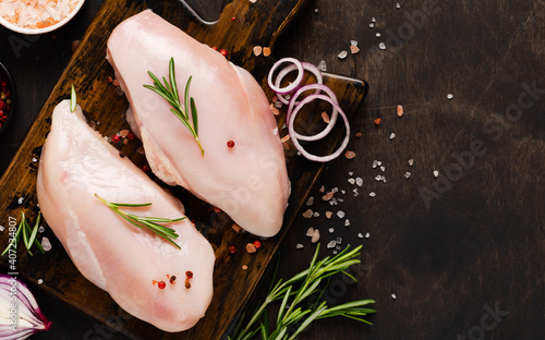 Raw chicken fillet with spices and herbs on dark cutting board. Cooking chicken breast background. Preparation food, Diet healthy meat. Top view.