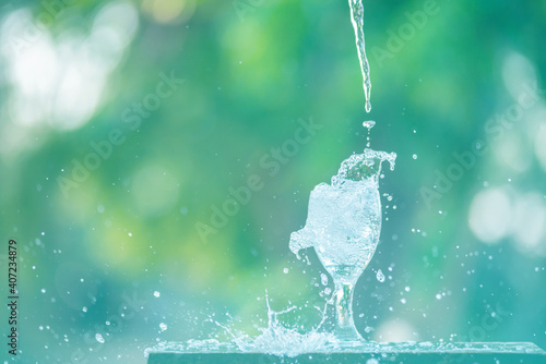 Water splash in glass Select focus blurred background.Drink water pouring in to glass over sunlight and natural green background.Nature conservation concept.