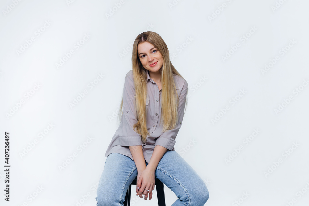 beautiful cute girl smiling sits on a chair in the studio, dressed in jeans and a blouse with blond long hair. beautiful cute girl smiling sits on a chair in the studio, dressed in jeans and a blouse with blond long hair.