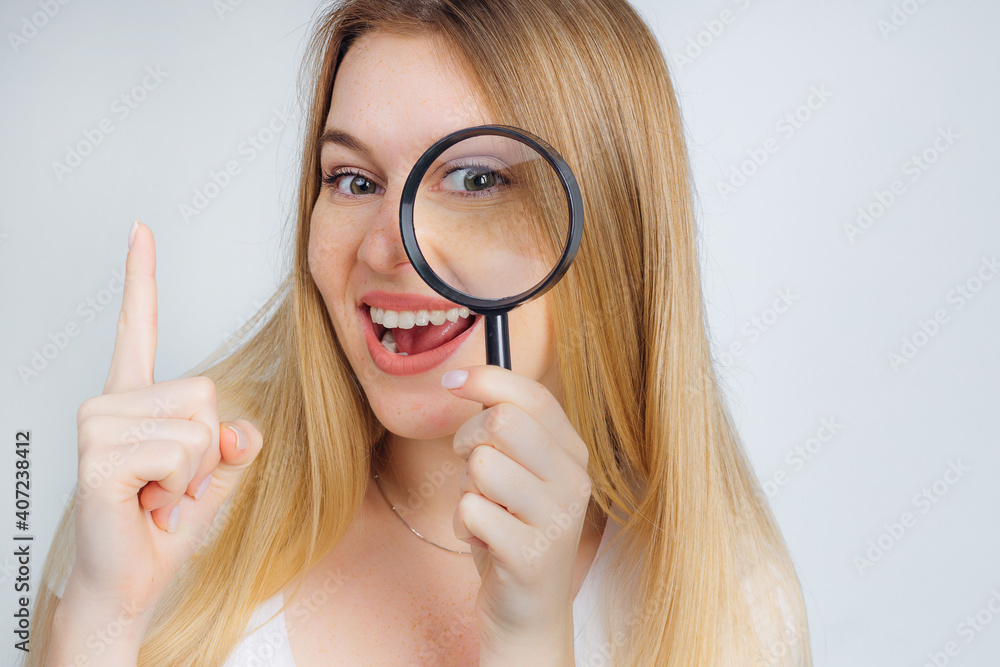 the girl looks through a magnifying glass with a smile, raises her thumbs up, she has found a solution to the problem. the girl looks through a magnifying glass with a smile, raises her thumbs up, she has found a solution to the problem.