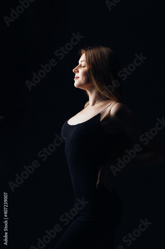 silhouette profile studio portrait of young beautiful fashion model with elegant black dress, holding her hands at the waist