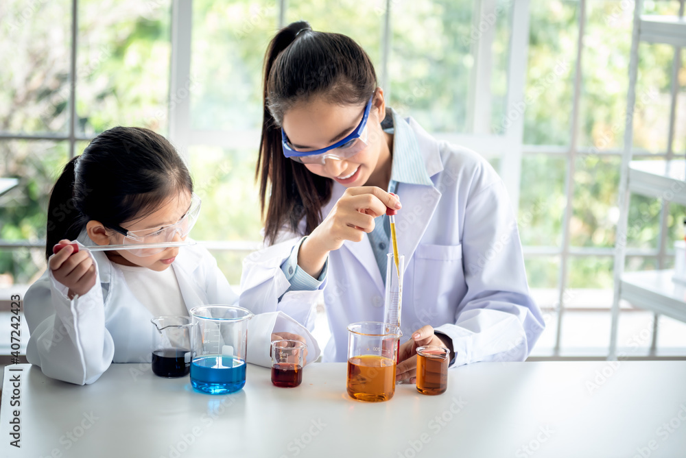 Blurred soft images of pretty Asian teacher is teaching a 6 year old girl, about scientific experiments On white table in a science lab classroom, to children and education concept. Blurred soft images of pretty Asian teacher is teaching a 6 year old girl, about scientific experiments On white table in a science lab classroom, to children and education concept.
