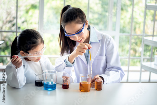 Blurred soft images of pretty Asian teacher is teaching a 6 year old girl, about scientific experiments On white table in a science lab classroom, to children and education concept.