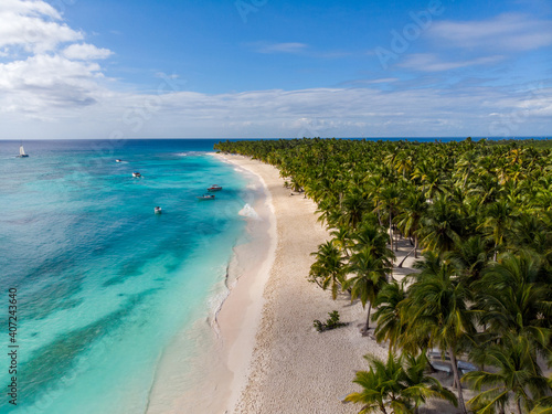 Aerial drone view of the paradise beach with palm trees, boats, sun beds, coral reef and blue water of Caribbean Sea, Saona island, Dominican Republic