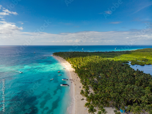 Aerial drone view of the paradise beach with palm trees  boats  sun beds  coral reef and blue water of Caribbean Sea  Saona island  Dominican Republic