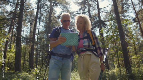Senior tourists couple on walk in forest using map on tablet. © nimito