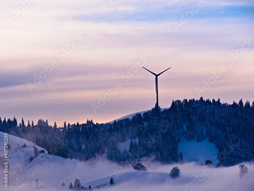 Schneebedeckte Hügellandschaft mit Wald und Windkraftanlage an einem bewölkten Wintertag in der Gemeinde Schwarzenberg im Kanton Luzern in der Schweiz