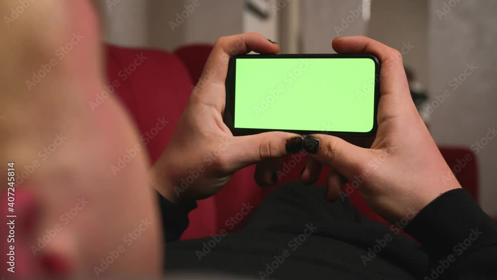 Back view. Close up homosexual man with manicure holding chromakey green screen smartphone watching content, play game, swiping scrolling on sofa couch at home. Gadgets people concept. Back view. Close up homosexual man with manicure holding chromakey green screen smartphone watching content, play game, swiping scrolling on sofa couch at home. Gadgets people concept.