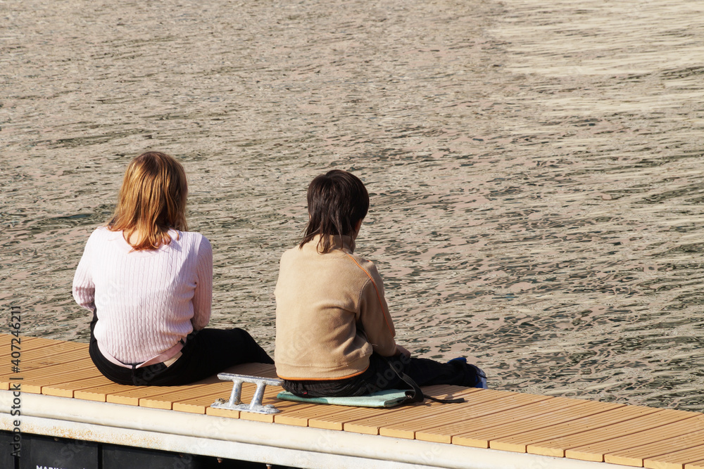 boy and girl sitting on the pier, back view