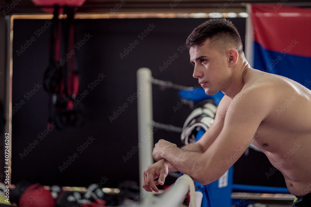 Young handsome kick boxer resting after training hard  and preparing for fight. Fighter working out at gym