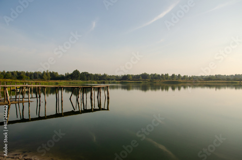 Old piers are reflected in the water of the lake. The sky is reflected in the water surface. Morning landscape. Peace and quiet in the countryside.